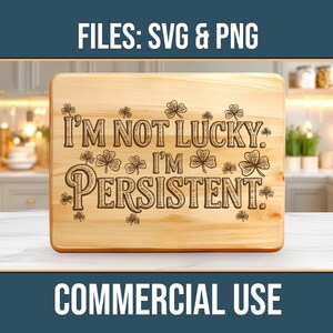 Puede incluir: Una tabla de cortar de madera clara con la frase grabada "I'M NOT LUCKY. I'M PERSISTENT." y diseños de tréboles. La tabla está sobre una superficie blanca. También se ven los textos "FILES: SVG & PNG" y "COMMERCIAL USE".