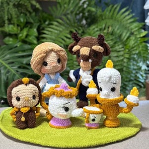 Puede incluir: Una colección de muñecos de ganchillo hechos a mano inspirados en los personajes de La Bella y la Bestia. Los muñecos incluyen a Bella, Bestia, Lumiere, Ding Dong, Sra. Potts y Chip. Cada muñeco presenta costuras detalladas y colores vibrantes, sobre una alfombra verde de ganchillo.