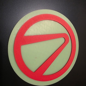 May include: A circular, pale green object featuring a red, stylized letter "7" design. The red design is encircled. The object is set against a black background.
