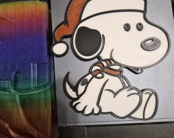 May include: A white and black cartoon dog ornament wearing a brown Santa hat and scarf. The dog is sitting down with its tail curled up. The ornament is likely for Christmas or holiday decor.