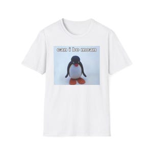 Könnte beinhalten: Weißes T-Shirt mit einem Pinguin-Motiv und dem Text "can i be mean". Der Pinguin hat einen schwarzen Kopf, einen weißen Körper, schwarze Flügel und orangefarbene Füße. Ein lässiges Kleidungsstück für den Alltag.