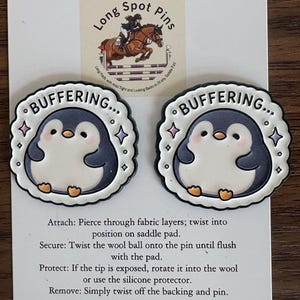 Peut inclure: Deux épinglettes rondes en émail représentant un pingouin de dessin animé avec un ventre blanc et un dos gris foncé. Le texte "BUFFERING..." est imprimé en haut de chaque épinglette, entouré de petites étoiles. Elles sont sur un support blanc.