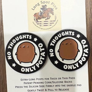 May include: Two black and white enamel pins with a brown potato character and the text "NO THOUGHTS ONLY POTATO". The pins are on a white card with text and a logo of a horse jumping over a fence.