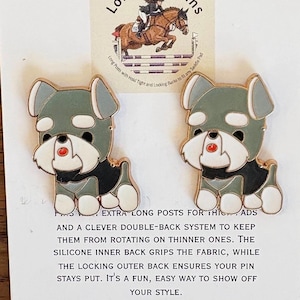 May include: Two dog-shaped enamel pins with gray, white, black, and red accents. The pins have a gold-colored outline. The pins are on a white card with text and a logo for Long Spot Pins.