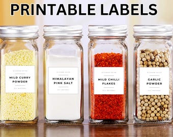May include: Four glass jars with silver lids, each filled with different spices and labeled. The labels read "Mild Curry Powder," "Himalayan Pink Salt," "Mild Chilli Flakes," and "Garlic Powder." The text "Printable Labels" is at the top.
