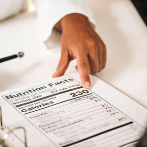 May include: A close-up of a nutrition facts label with the text "Nutrition Facts" at the top. The label shows the number of calories per serving, with a hand pointing to the number 230. A pen is also visible.