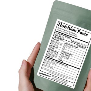 May include: A green pouch with a nutrition facts label, held by a hand. The label details calories, macronutrients, and micronutrients. Ingredients include rice flour, coconut water, agave syrup, and pistachios.