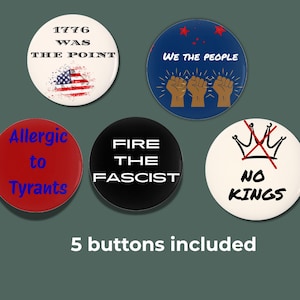 May include: Five circular buttons with political slogans. The buttons display phrases such as "1776 WAS THE POINT," "WE THE PEOPLE," and "NO KINGS." The colours are red, white, blue, and black.