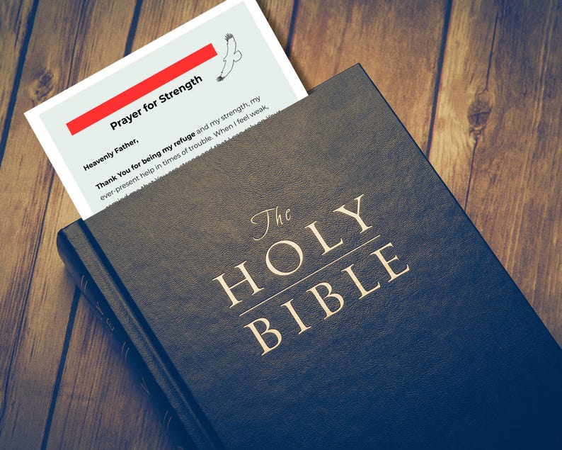 Pode incluir: Uma B&iacute;blia azul escura com letras douradas que dizem "The Holy Bible". Um marcador com o texto "Prayer for Strength" e um desenho de um p&aacute;ssaro &eacute; inserido. A B&iacute;blia est&aacute; sobre uma superf&iacute;cie de madeira.