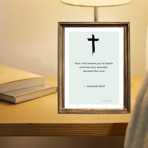 Puede incluir: Una impresi&oacute;n enmarcada con una cruz negra y la cita "Pero yo te restaurar&eacute; la salud, y sanar&eacute; tus heridas, dice el Se&ntilde;or." de Jerem&iacute;as 30:17. El marco es de color marr&oacute;n oscuro. Dos libros est&aacute;n sobre una superficie de madera.