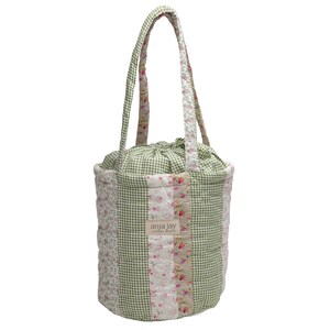 May include: A quilted tote bag with a drawstring closure and matching handles. The bag features a patchwork design with green gingham, floral, and solid fabric panels. The bag has the text "anja jay" on the front.