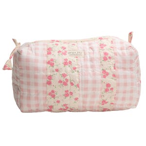 May include: A quilted, rectangular travel bag with a pink and white gingham pattern. The bag features a central panel with a floral rose print and the brand name "anja jay". The bag has small fabric loops on each end.