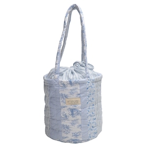 May include: A quilted tote bag with a drawstring closure and matching handles. The bag features a patchwork design in shades of blue and white, with floral and striped patterns. The label "anja jay" is visible.