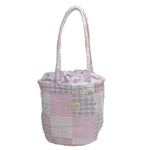 May include: A patchwork tote bag with a drawstring closure and matching handles. The bag features a variety of pink, white, and floral patterned fabrics. The label "anja jay" is visible on the front of the bag. The bag is approximately 12 inches tall.
