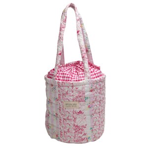 May include: A quilted tote bag with a floral and gingham pattern. The bag features a drawstring closure and two handles. The exterior is a mix of pink floral and white and pink gingham fabric. The bag has a label that reads "anja jay london beach".