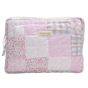 May include: A rectangular, quilted cosmetic bag with a patchwork design. The bag features various pink and white patterned squares, including floral, polka dot, and striped fabrics. The label reads "anja jay laguna beach". A zipper and tassel detail the side.