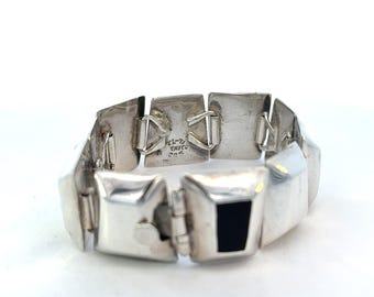 May include: A silver-toned bracelet with geometric, square-shaped links. One link features a black, rectangular inlay. The bracelet is marked "Mexico" and "925".
