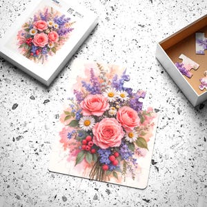 以下が含まれることがあります： ピンクのバラ、白いヒナギク、紫のラベンダーの花束が描かれた花のパズル。 パズルは部分的に組み立てられており、近くにピースが散らばっています。 白いパズルボックスには、同じ花の模様が蓋にあります。 「custom made」の文字が見えます。