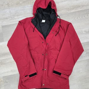 May include: A red hooded jacket with a black interior lining. The jacket has a button-up front, adjustable cuffs, and a drawstring hood. The jacket is made of a durable material and is suitable for outdoor activities.