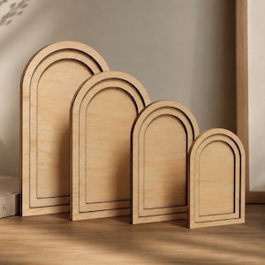 May include: A set of four light-colored wooden arch-shaped plaques arranged in descending order of size. Each plaque features a smooth, flat surface with a raised, arched border frame, showcasing the natural grain and texture of the wood material.