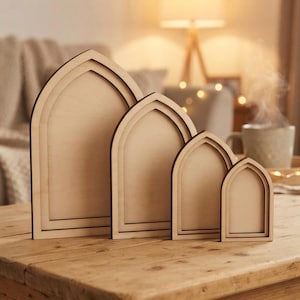 May include: A set of four light-colored wooden arch-shaped frames arranged in descending order of size. Each frame features a smooth, flat surface with a distinct arched top and a layered border design, crafted from natural wood with a light grain.