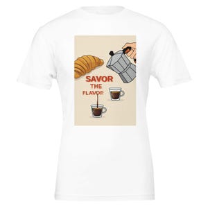 May include: White t-shirt with a graphic of a croissant, coffee, and a coffee maker. The words "Savor the Flavor" are printed in red. The image shows coffee being poured into a cup.