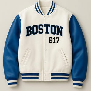 Puede incluir: Chaqueta universitaria color crema con mangas azules. La chaqueta presenta la palabra "BOSTON" en letras de bloque azul marino, junto con el número "617". El cuello, los puños y el dobladillo tienen detalles a rayas azules y blancas.