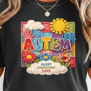 Puede incluir: Camiseta negra con un diseño de patchwork colorido con la palabra "AUTISMO" en el centro. El diseño incluye flores, un sol y las palabras "ACEPTAR COMPRENDER AMAR" en una nube. La camiseta tiene cuello redondo.