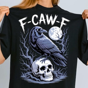 Puede incluir: Camiseta negra con un diseño de un cuervo sobre una calavera, con una luna llena y árboles desnudos de fondo. El diseño incluye el texto "F-CAW-F" en una fuente llamativa, creando un tema gótico.