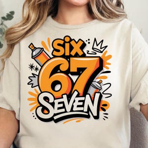 Könnte beinhalten: Cremefarbenes T-Shirt mit einem lebendigen Grafikdesign. Das Design enthält das Wort "Six" über der Zahl "67" und das Wort "Seven" in einer kräftigen, stilisierten Schriftart. Orangefarbene Sprühdosen und eine Krone sind ebenfalls enthalten.