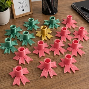 May include: A collection of colorful candle holders in shades of pink, green, and yellow, arranged on a wooden surface. The candle holders have a ribbon-like design. A framed sign with the text "CREATE PRINT INSPIRE" is also visible.
