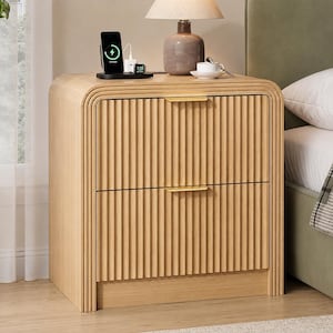 May include: A light wood nightstand featuring two drawers with vertical fluted detailing and slim gold-toned horizontal handles. The top surface holds a table lamp with a beige shade, a black wireless charging stand, and a small white cup.