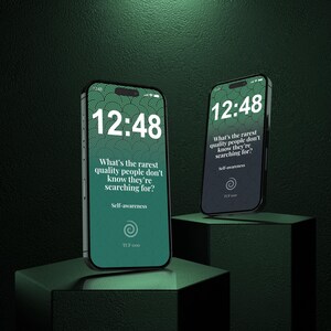以下が含まれることがあります： 12:48の時刻と「What's the rarest quality people don't know they're searching for?」と「Self-awareness」のテキストが表示された、緑と黒のグラデーション画面のスマートフォン2台。スマートフォンは濃い緑色の台座に置かれています。