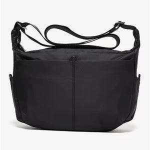 May include: A black messenger bag with a textured exterior. The bag features a long, adjustable shoulder strap and multiple pockets, including two side pockets and a large front pocket. The bag is designed for carrying items.