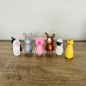 May include: Set of six wooden figurines painted to resemble farm animals. The figurines include a cow, pig, donkey, chicken, sheep, and a grey rabbit. The figurines are all standing upright and are painted in bright colors.