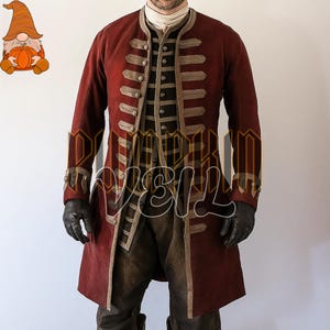 May include: A burgundy-colored, long-sleeved coat with gold trim and buttons. The coat has a high collar and is paired with a vest and dark pants. Black gloves complete the ensemble, creating a historical or theatrical look.