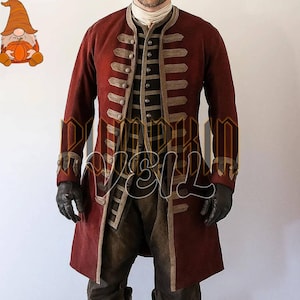 Può includere: Un cappotto lungo rosso scuro con finiture decorative color marrone chiaro e asole orizzontali sul davanti. È indossato sopra un gilet a righe orizzontali scure, una camicia chiara a collo alto, pantaloni scuri e guanti neri.