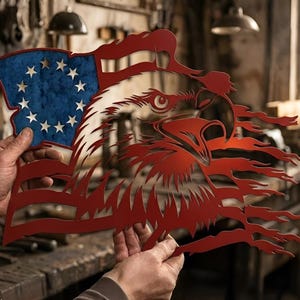 May include: A red, white, and blue metal art piece depicting an American flag with an eagle's head. The flag features a blue field with white stars and red and white stripes. The eagle's head is in the center, with a white and red design.