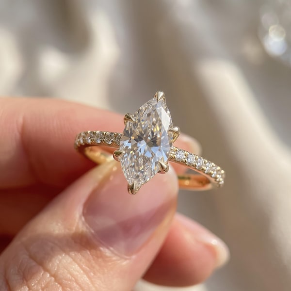Puede incluir: Un anillo de oro con una gran piedra central de talla marquesa sujeta por seis garras. El aro está fabricado en oro amarillo y decorado con una hilera de pequeñas piedras blancas redondas de talla brillante a ambos lados de la gema.