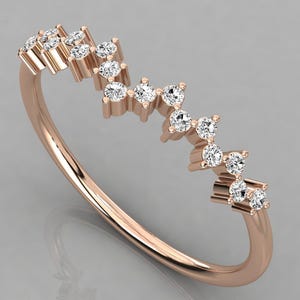 May include: Rose gold ring with a delicate design. The ring features a series of small, sparkling diamonds set in a zig-zag pattern across the top. The band has a smooth, polished finish. A beautiful piece of jewelry.