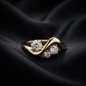 Può includere: Un anello in oro caratterizzato da una fascia liscia e ondulata che avvolge tre pietre rotonde, trasparenti e sfaccettate. La pietra più grande è incastonata in modo prominente su un lato, mentre due pietre più piccole sono raggruppate sul lato opposto.
