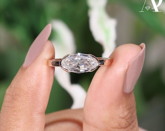 Può includere: Un anello d'oro con un diamante taglio marquise. Il diamante è incastonato in una montatura a castone. L'anello è tenuto tra due dita, su uno sfondo verde e bianco sfocato.