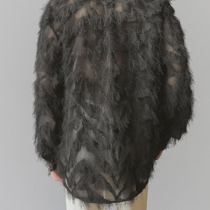 Puede incluir: Top negro de manga larga y texturizado con un dise&ntilde;o de plumas. La parte superior tiene una calidad transparente y se combina con pantalones color crema. La textura y el dise&ntilde;o de la prenda crean un atractivo visual &uacute;nico.