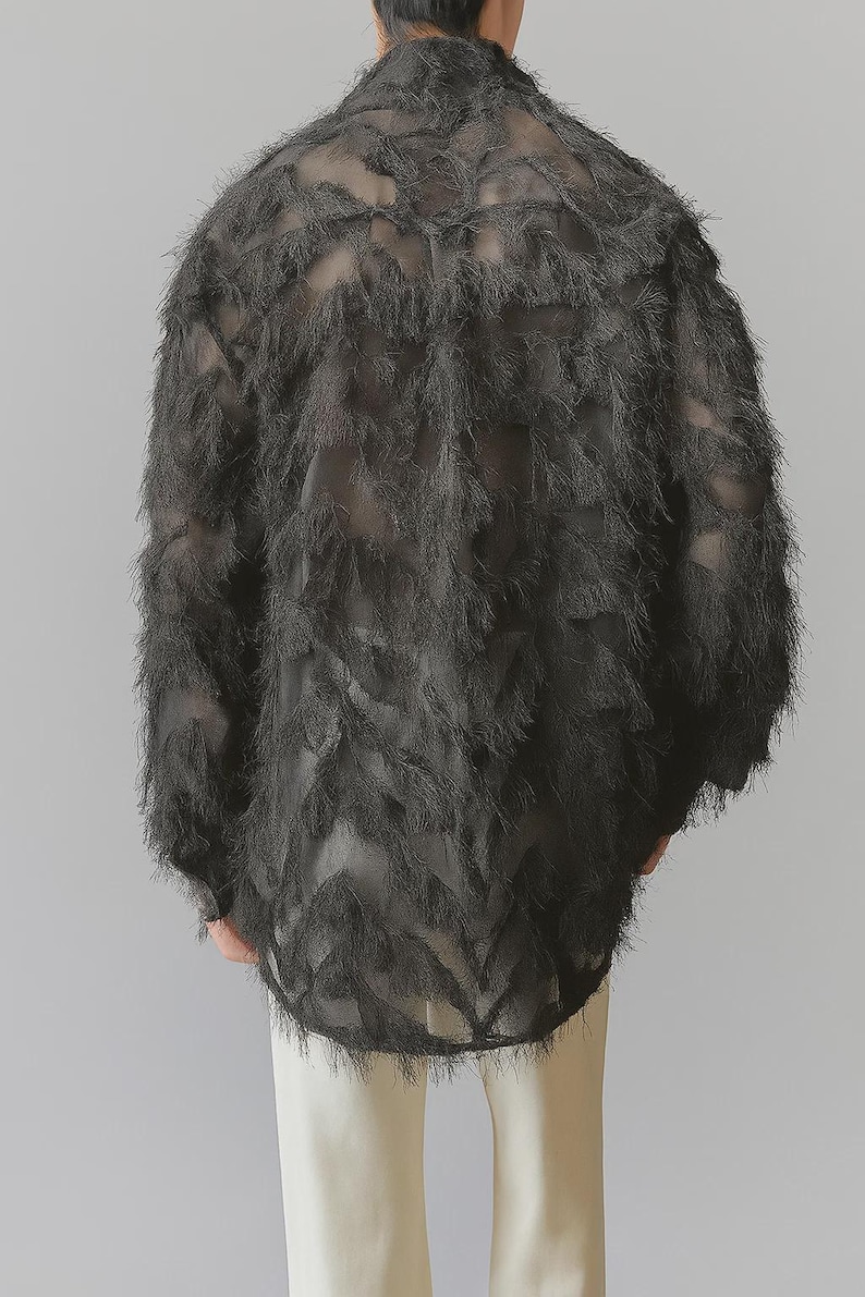 Puede incluir: Top negro de manga larga y texturizado con un dise&ntilde;o de plumas. La parte superior tiene una calidad transparente y se combina con pantalones color crema. La textura y el dise&ntilde;o de la prenda crean un atractivo visual &uacute;nico.