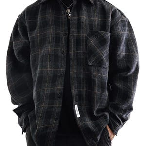 Op de afbeelding: Een donkergrijs geruit flanellen overhemd met een knoopsluiting aan de voorkant, een borstzak en een klein wit label. Het overhemd heeft een klassieke kraag en lange mouwen. Het ruitpatroon bevat bruine en zwarte lijnen.