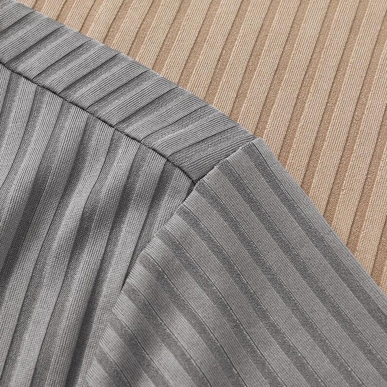 May include: Close-up of a gray ribbed fabric, possibly a top or dress, with a contrasting tan ribbed fabric in the background. The fabrics are angled, showing the texture and construction of the garment.