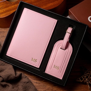 May include: A pink passport holder and luggage tag set, presented in a black gift box. Both items are embossed with the initials "MS" in gold. The set is made of a textured material and includes a luggage tag with a buckle.