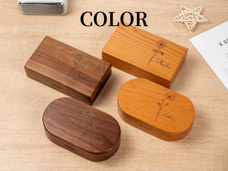 K&ouml;nnte beinhalten: Vier Holzkisten in verschiedenen Formen und Farben. Zwei sind rechteckig und zwei oval. Jede Box hat ein Blumendesign und einen Namen auf der Oberseite eingraviert. Das Wort "COLOR" ist oben im Bild in Schwarz gedruckt.
