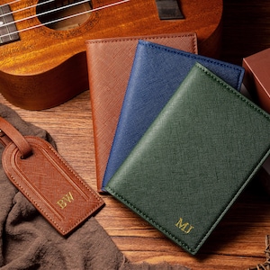 May include: A collection of leather goods, including a brown luggage tag with "BW" and three passport holders in brown, blue, and green, each with initials. A ukulele is in the background.
