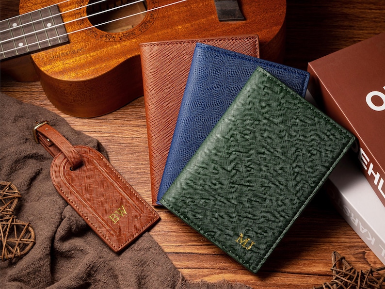 May include: A collection of leather goods, including a brown luggage tag with "BW" and three passport holders in brown, blue, and green, each with initials. A ukulele is in the background.